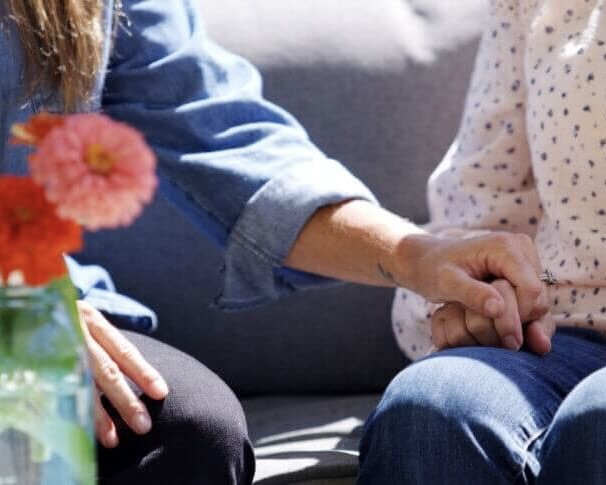 Photo of a woman and elderly woman holding a hand over the elderly womans lap
